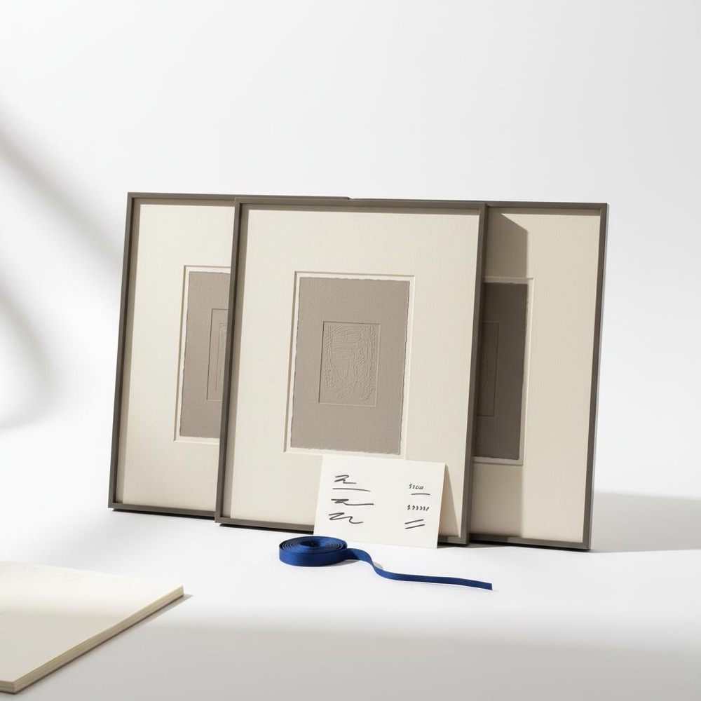 Close-up still life of framed prints on a white wall with a size-and-price label and a subtle #1a5bfb ribbon, highlighting paper texture and print quality for artist website platforms